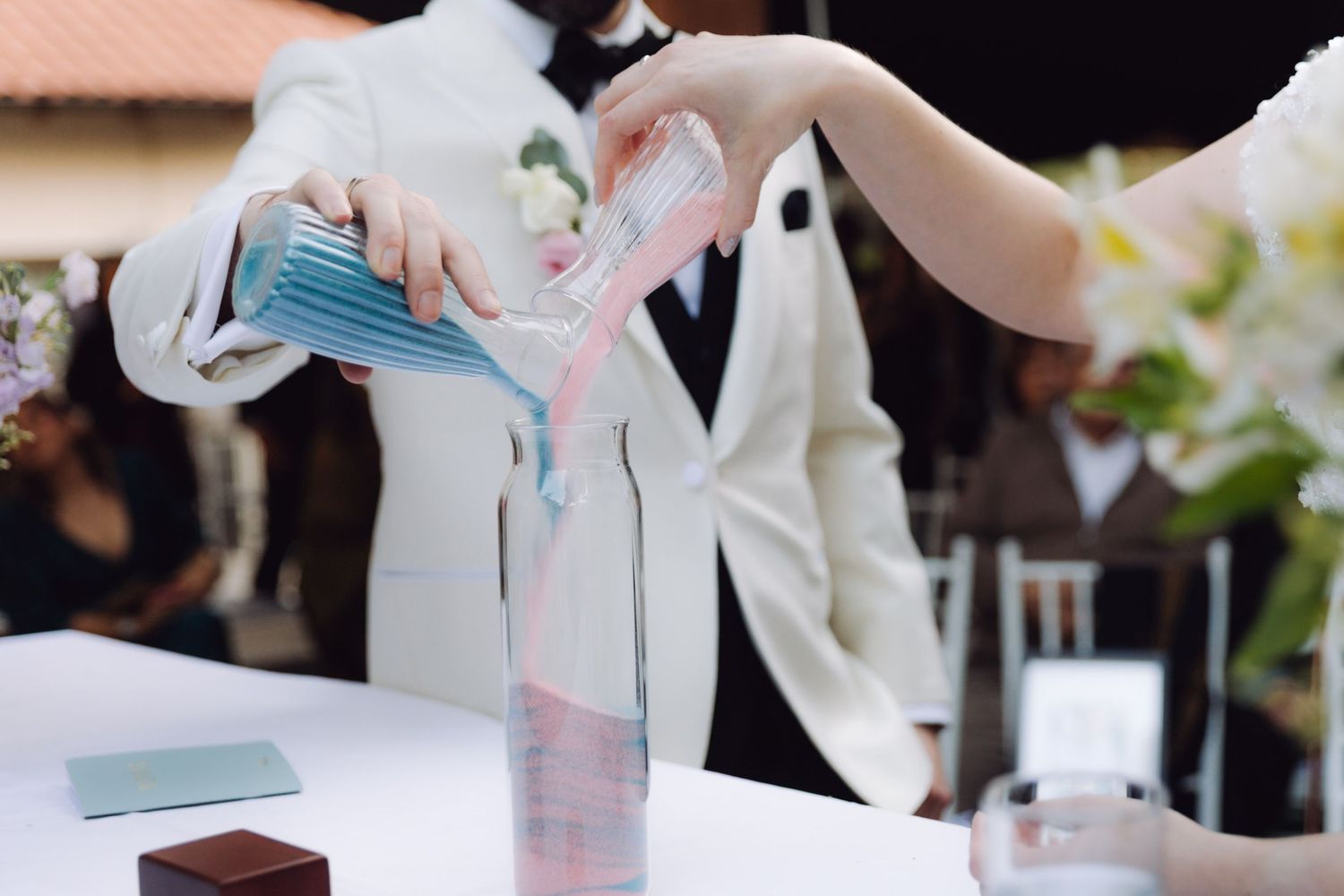 Close-up of bride and groom pouring blue and pink sand during a unity ceremony at their wedding.