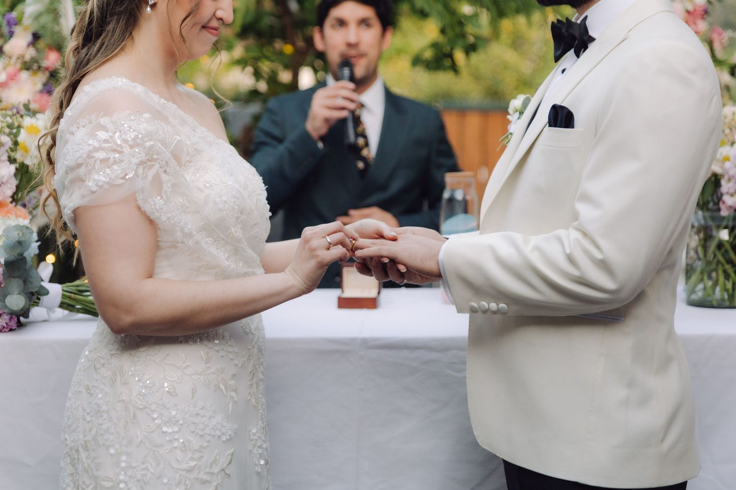 Bride places a wedding ring on the grooms finger during an outdoor garden wedding ceremony.