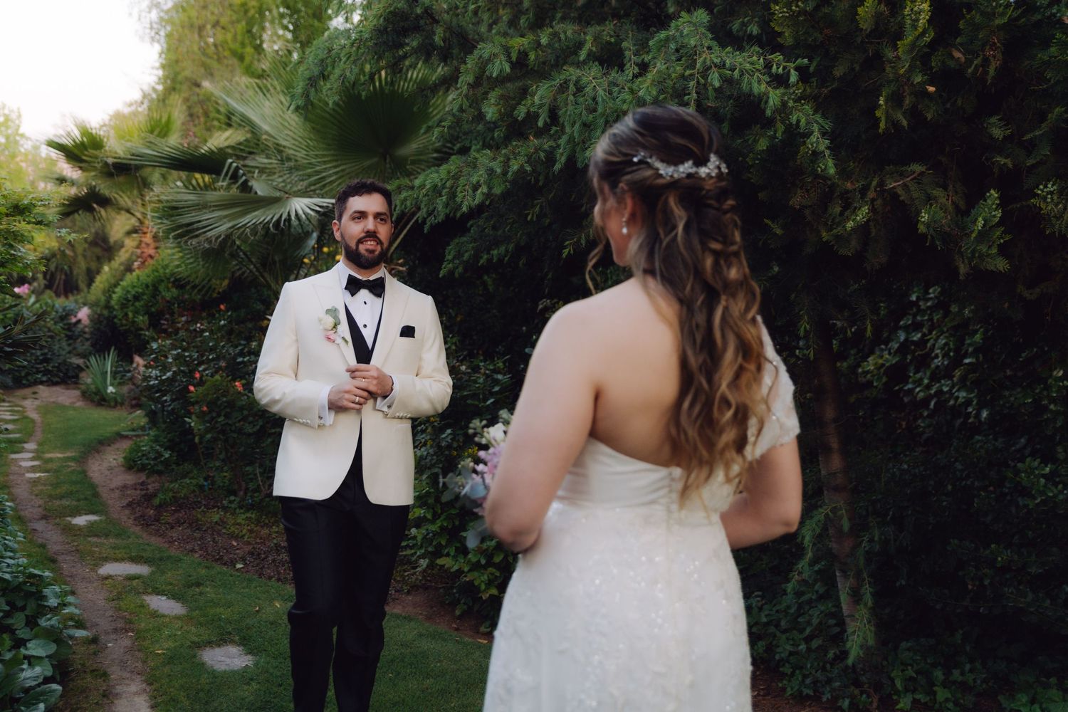 Groom in white tuxedo seeing bride for the first time during outdoor wedding first look.