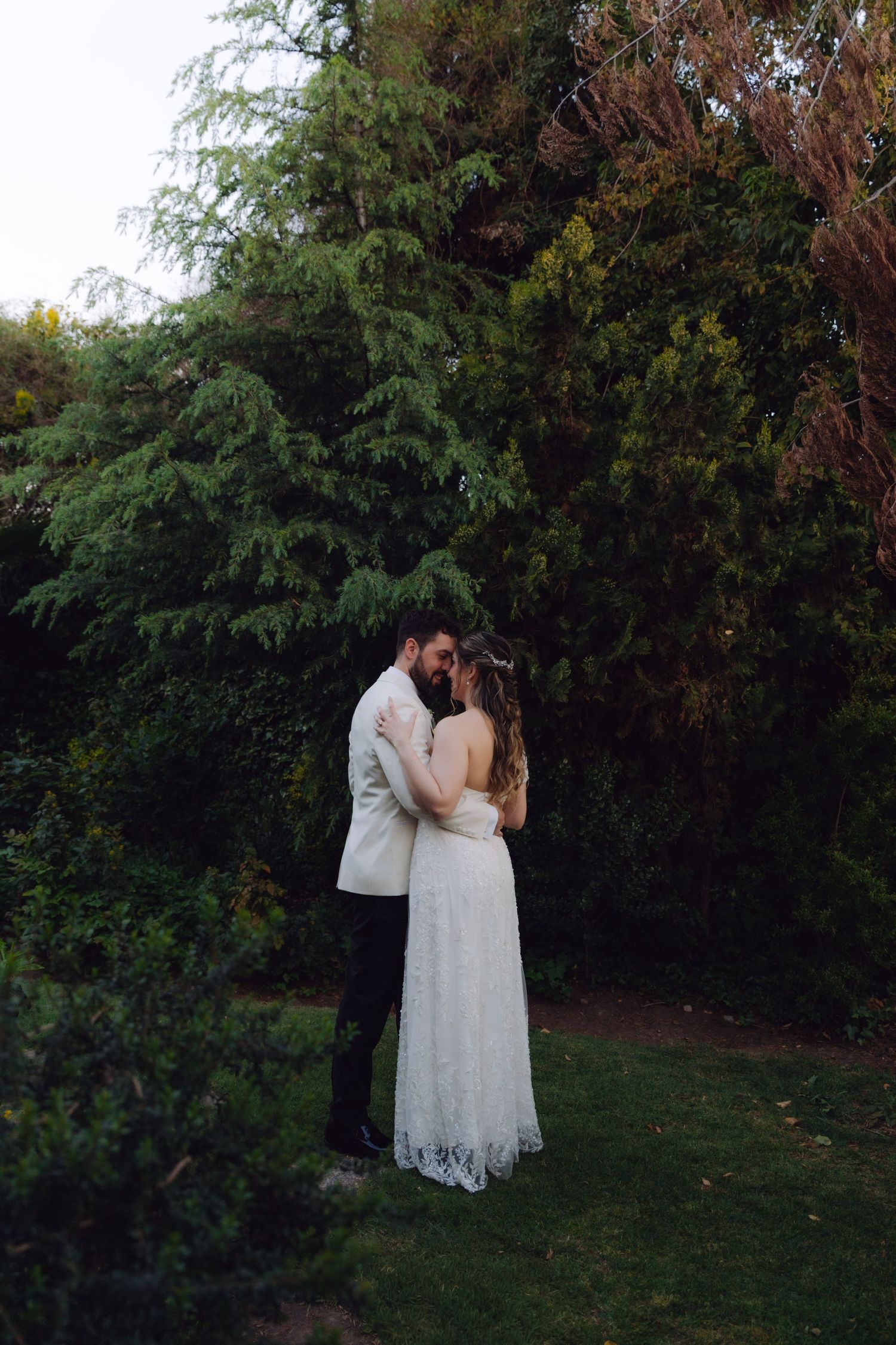 Bride and groom sharing a romantic kiss in a lush green garden at their wedding.