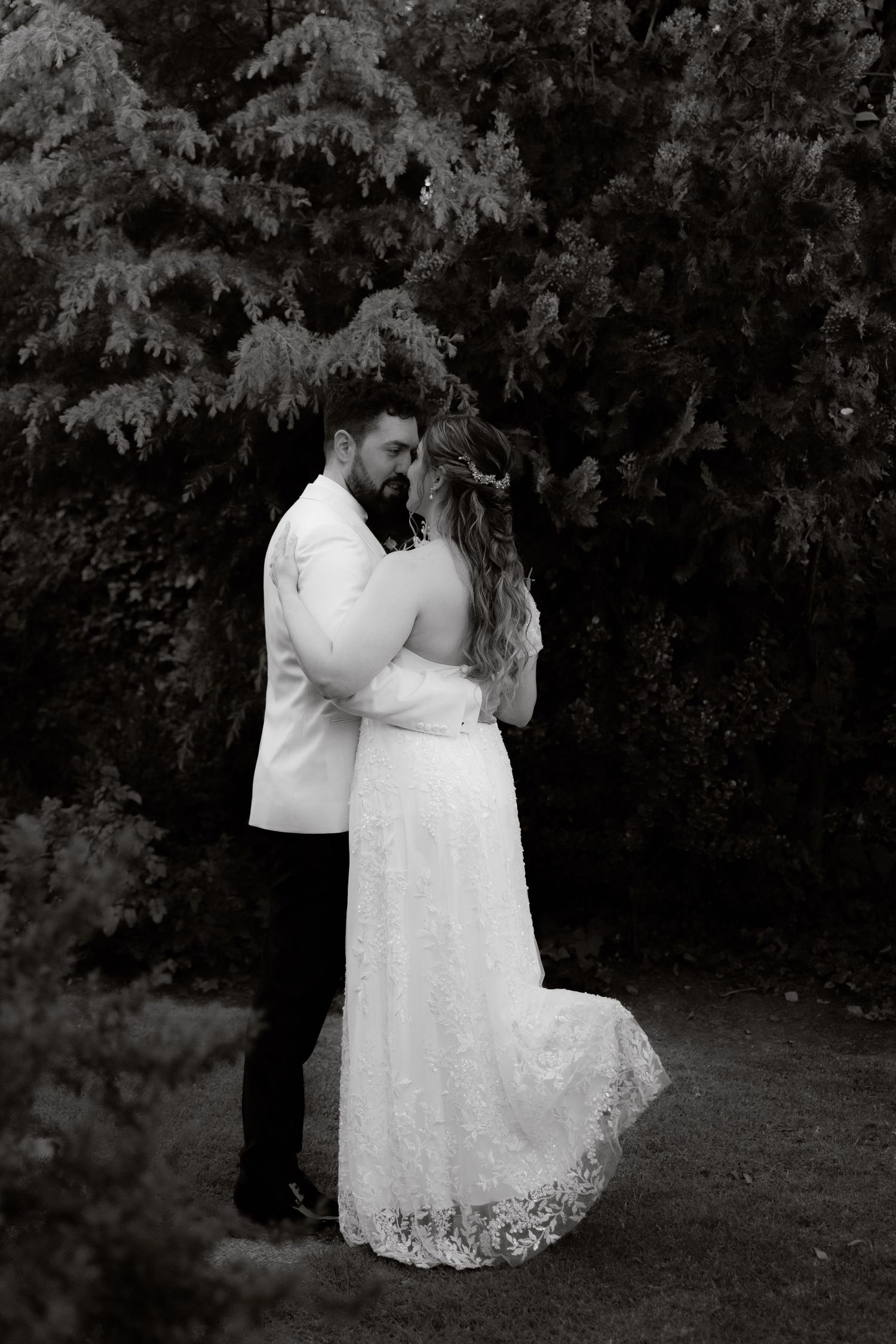 Black and white photo of bride and groom embracing tenderly in a garden setting.