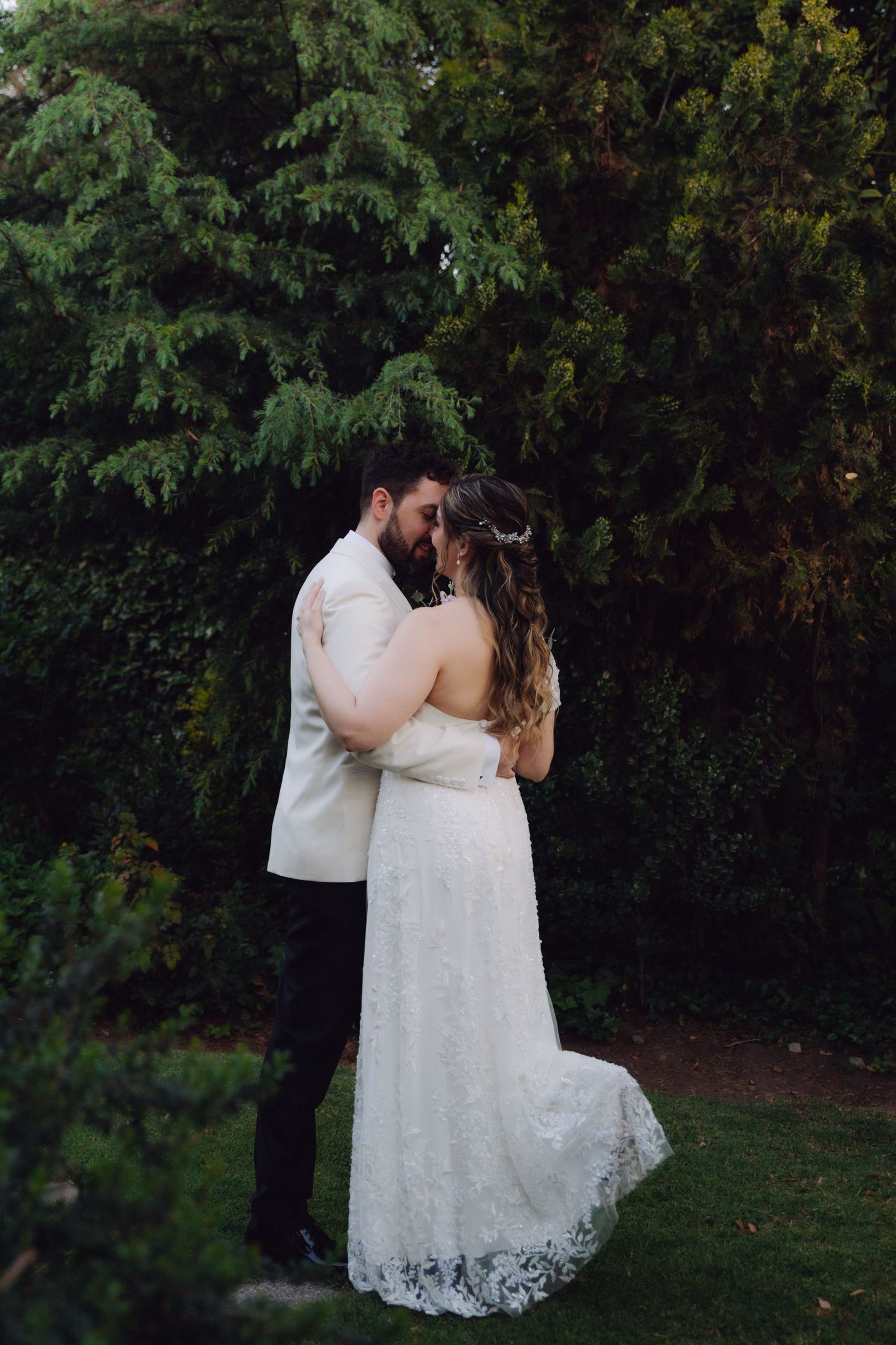 Bride and groom share a romantic kiss in a lush garden, bride wearing elegant lace wedding gown.