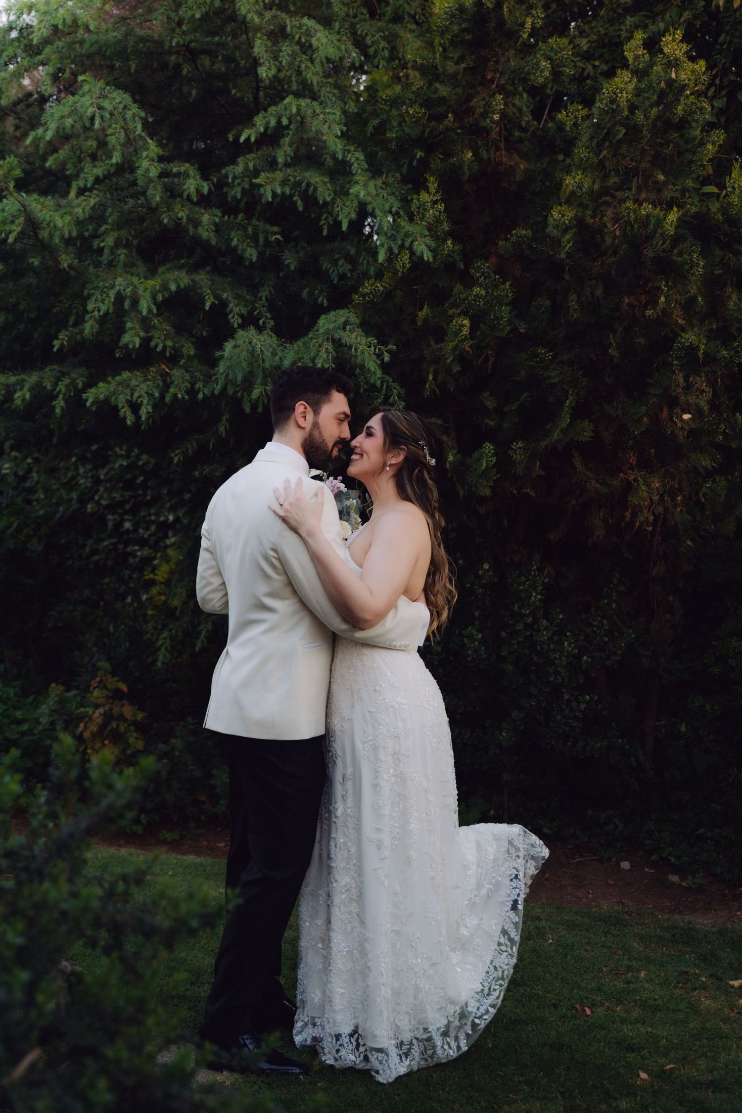 Smiling bride and groom embrace tenderly in a green garden setting during their wedding day.