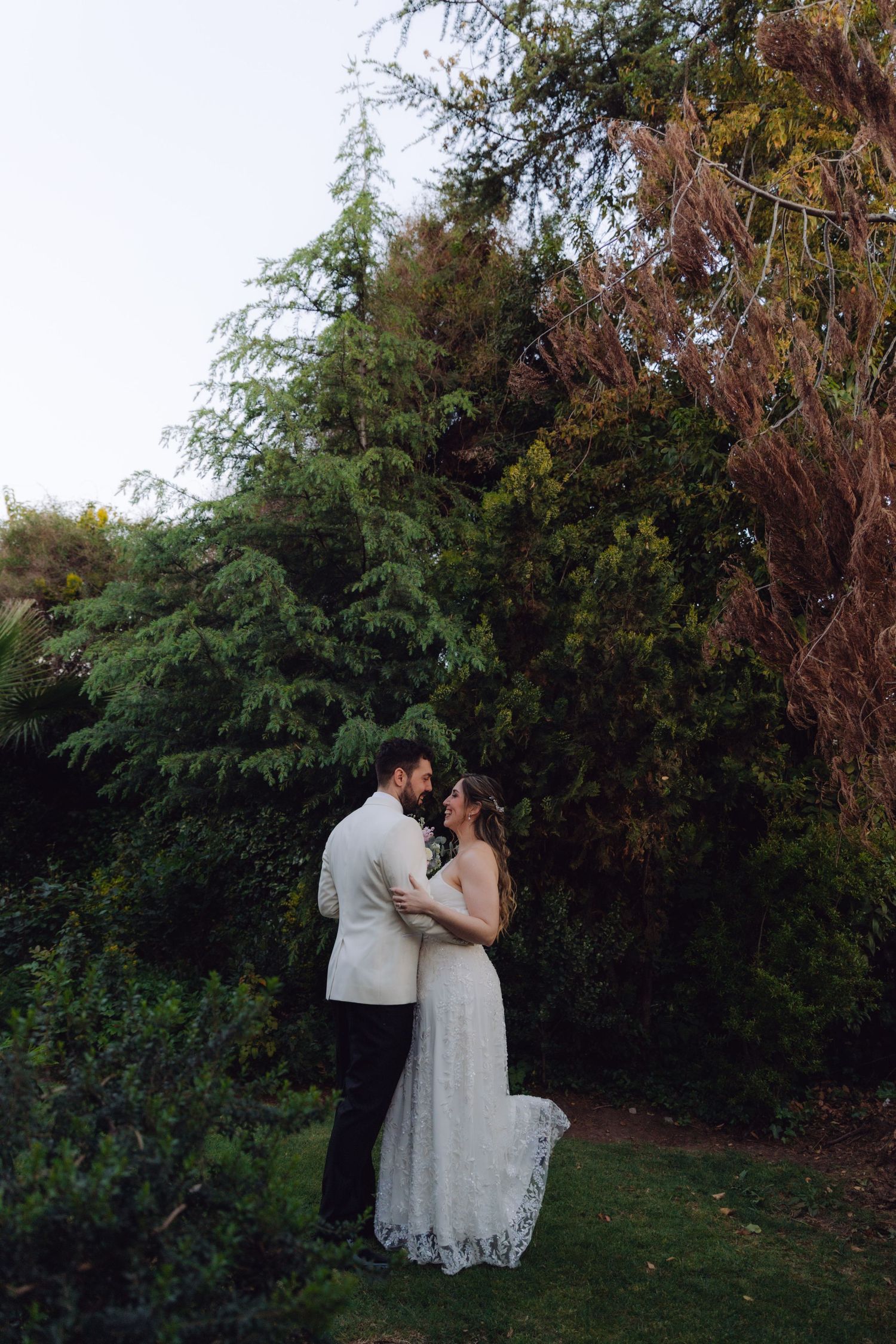 Wedding couple sharing an intimate moment surrounded by lush greenery and trees at dusk.