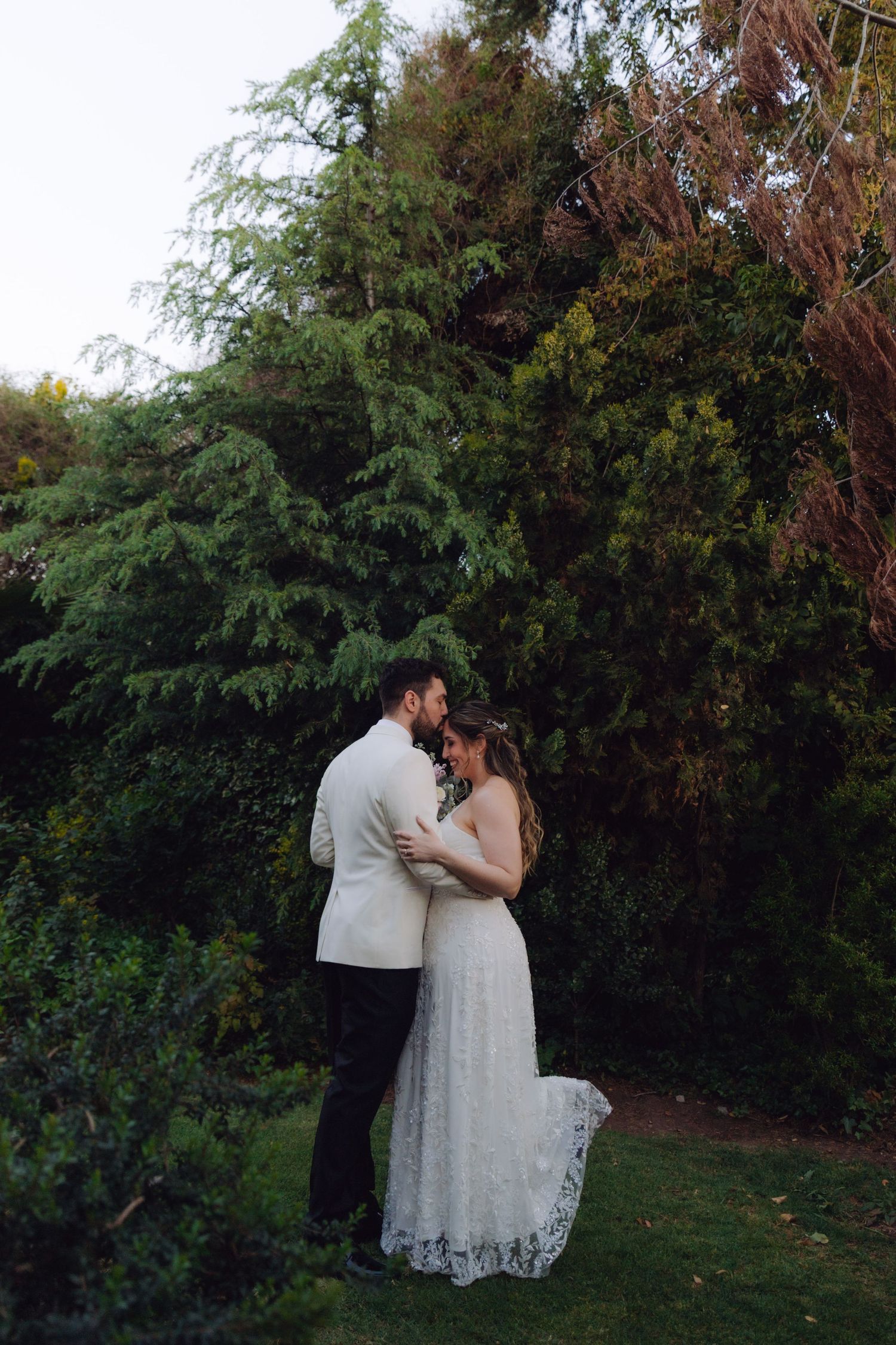 Bride and groom share a tender embrace in a lush garden at twilight on wedding day.