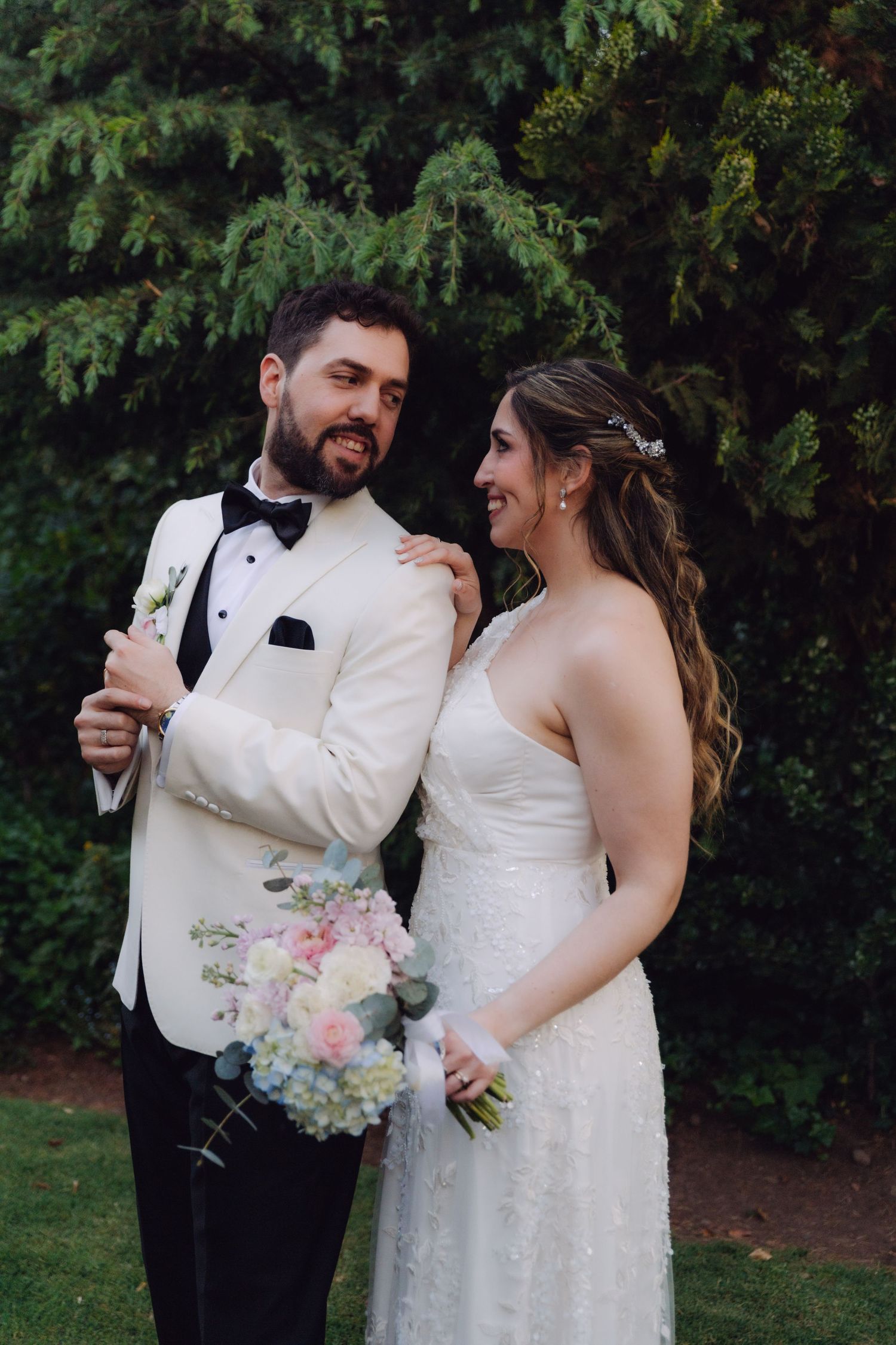 Laughing bride and groom pose together outdoors, bride holding pink and white floral bouquet.