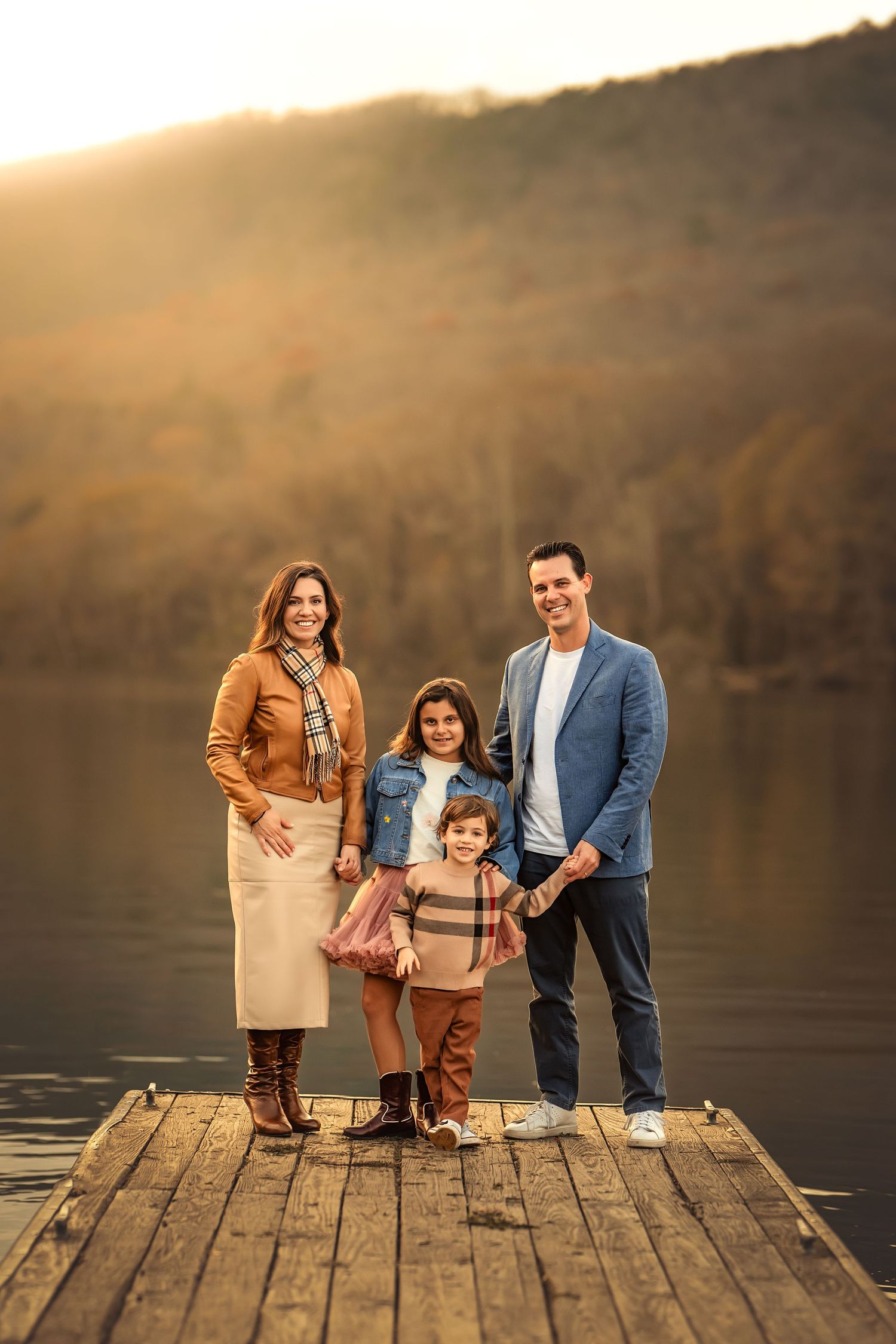 Family of four posing on a wooden dock by a lake during golden hour in autumn.