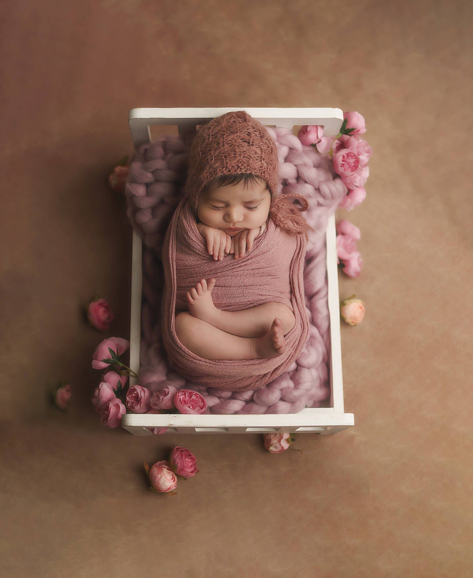 Sleeping newborn baby girl in pink bonnet and wrap in white wooden crib with pink roses.