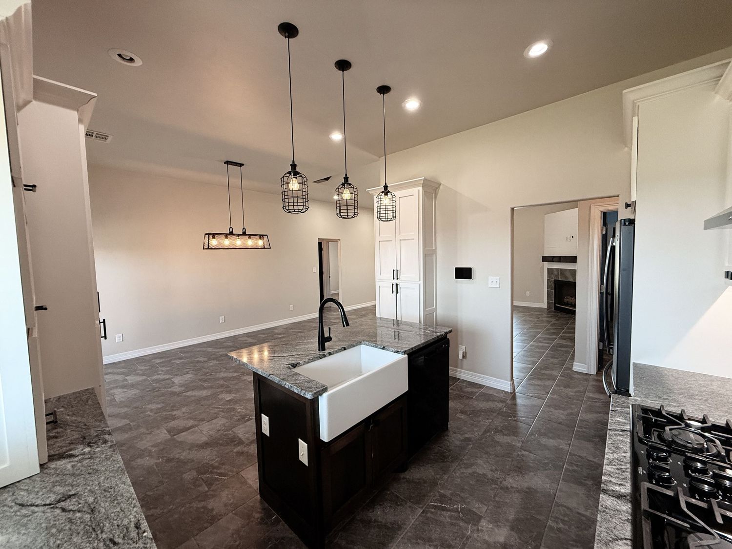 Modern kitchen with dark island featuring a farmhouse sink, pendant lights, and granite countertops.