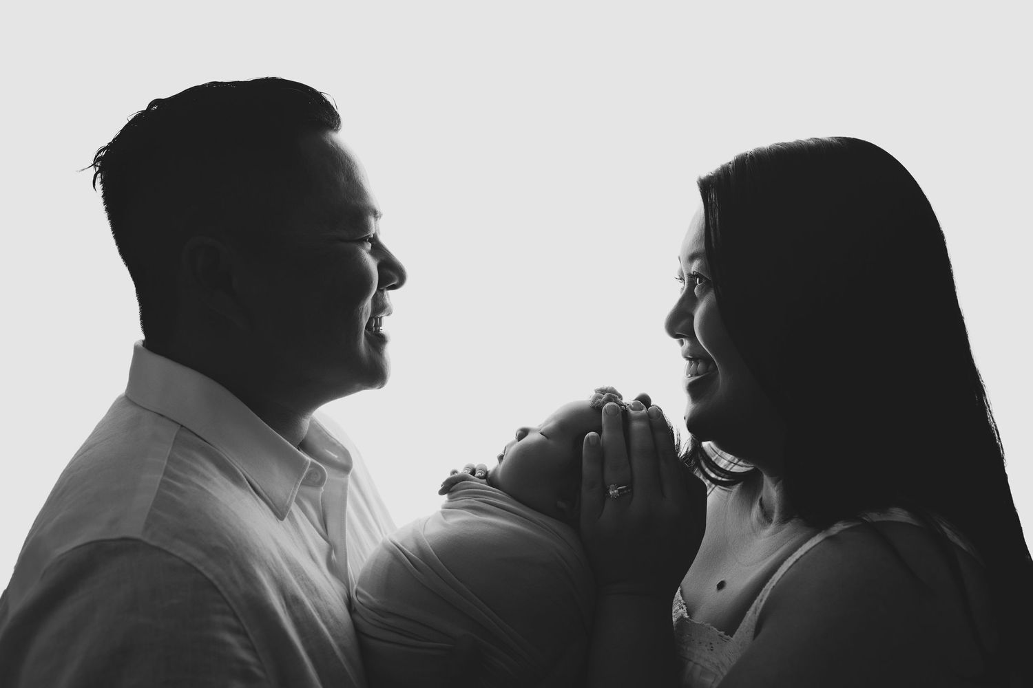 Black and white photo of smiling parents holding their newborn baby in a tender family portrait.