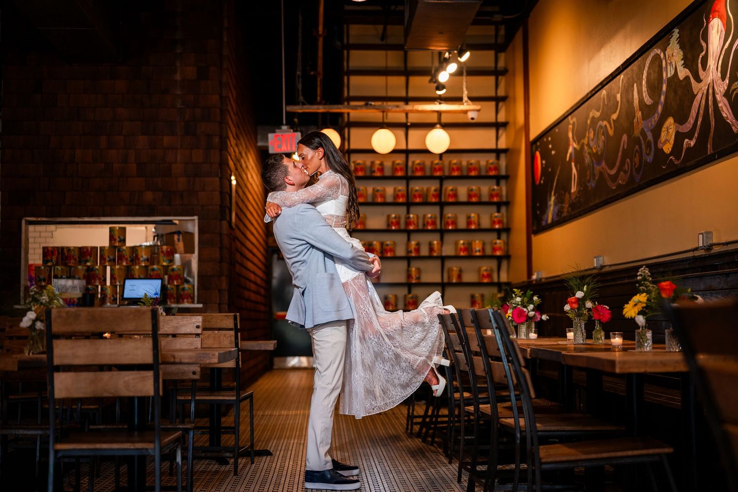Couple sharing a romantic lift and kiss inside a warmly lit restaurant with wooden decor and artwork.