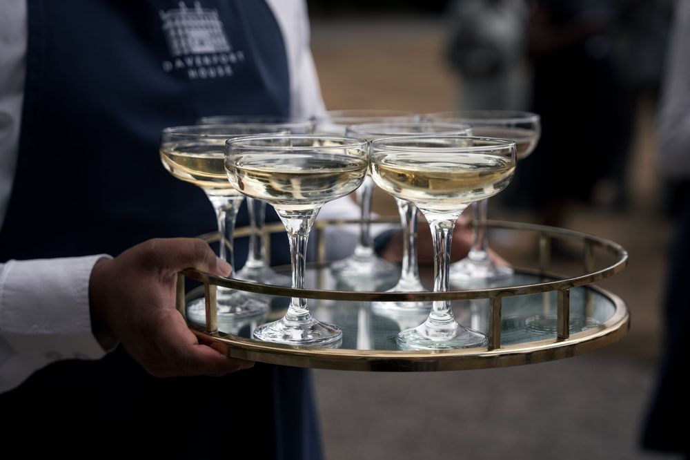 Waiter holding a gold mirrored tray with elegant coupe glasses filled with champagne at an outdoor event.