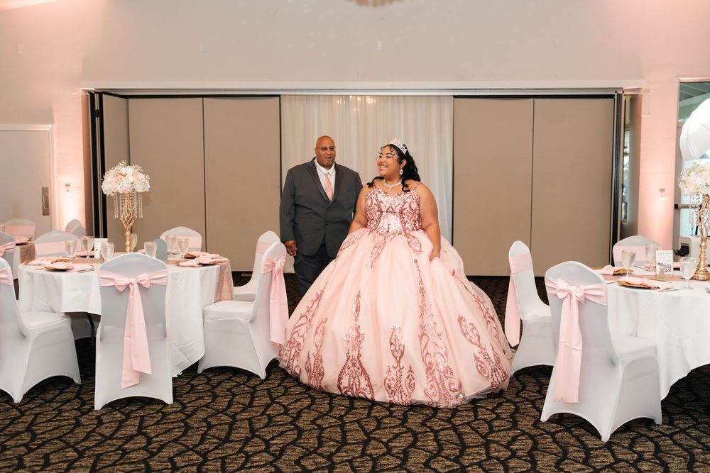 A young woman in a pink ballgown quinceañera dress poses with a man in a suit at an elegant banquet hall.