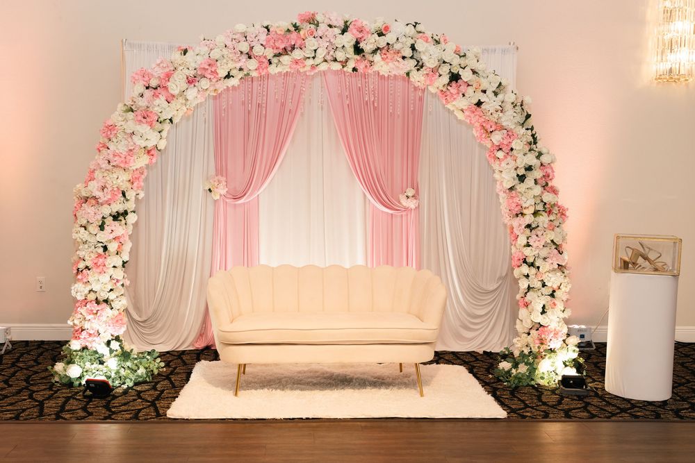 Elegant pink and white floral arch with cream loveseat centerpiece for quinceañera party decor.
