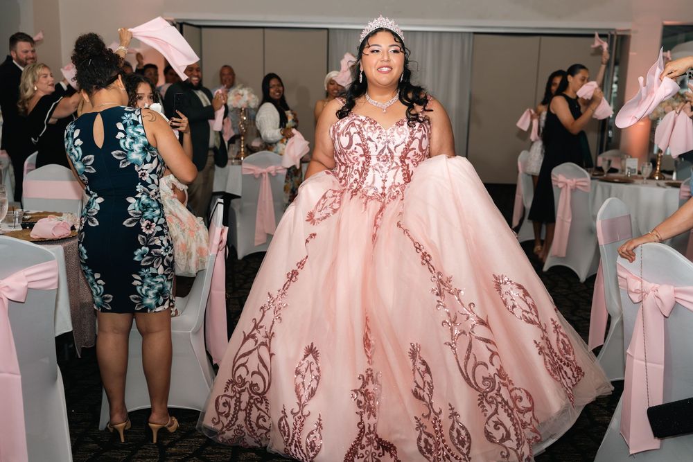 Young woman in pink quinceañera ball gown with floral embroidery celebrating her sweet 16 party.