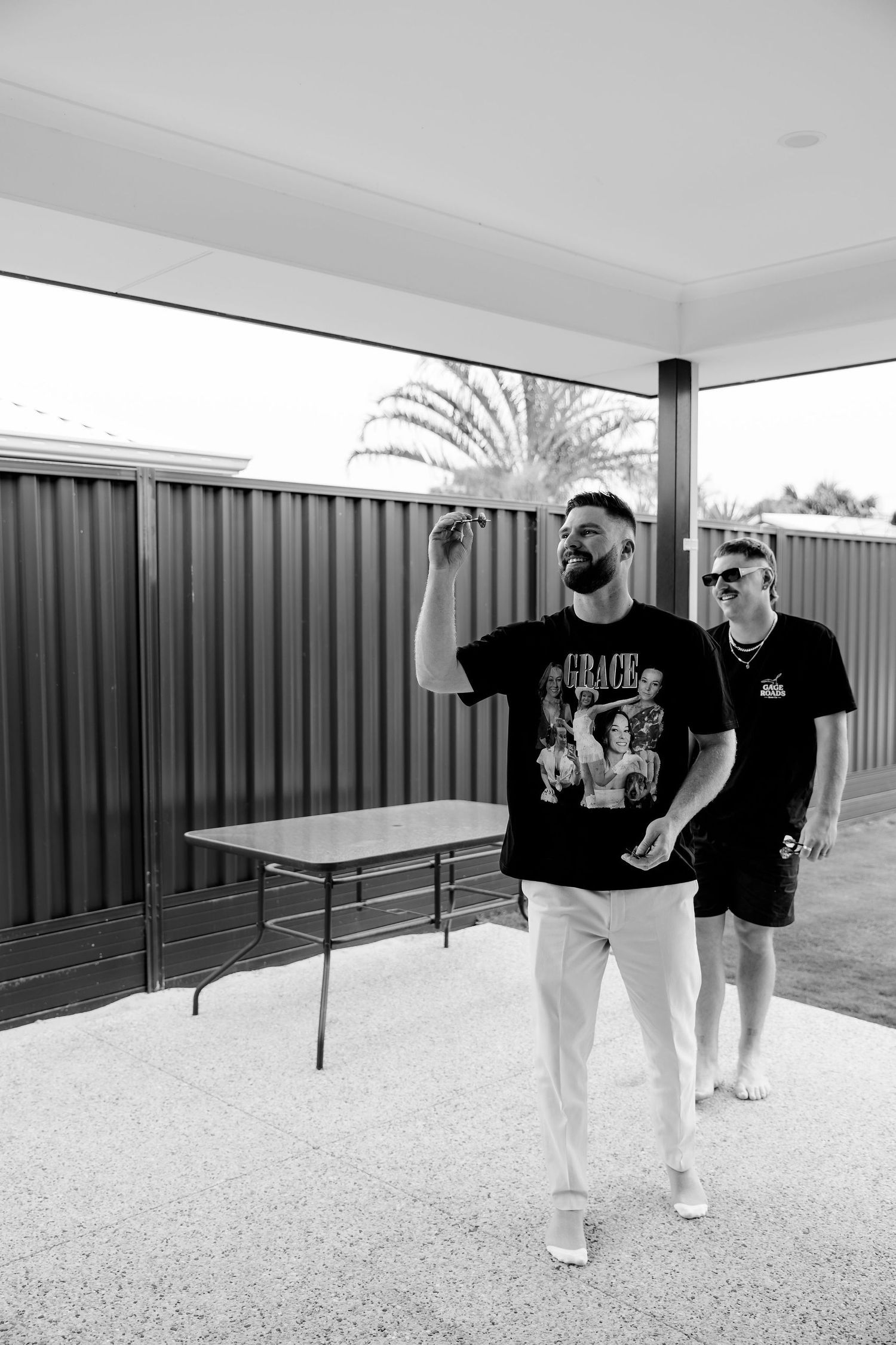 Two people walking together in black t-shirts and light pants along a covered outdoor walkway.