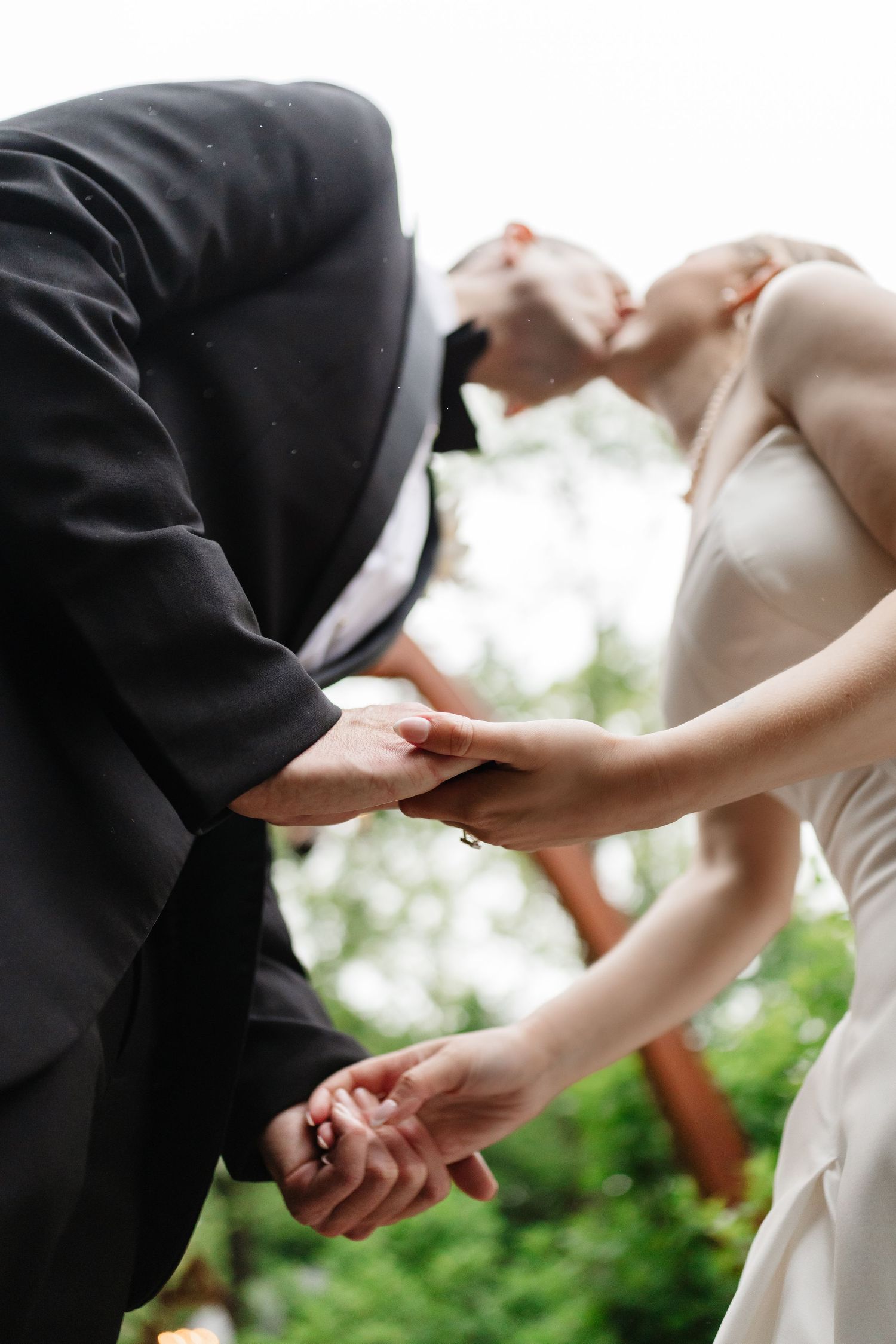 Bride and groom sharing romantic kiss while holding hands at outdoor wedding ceremony.