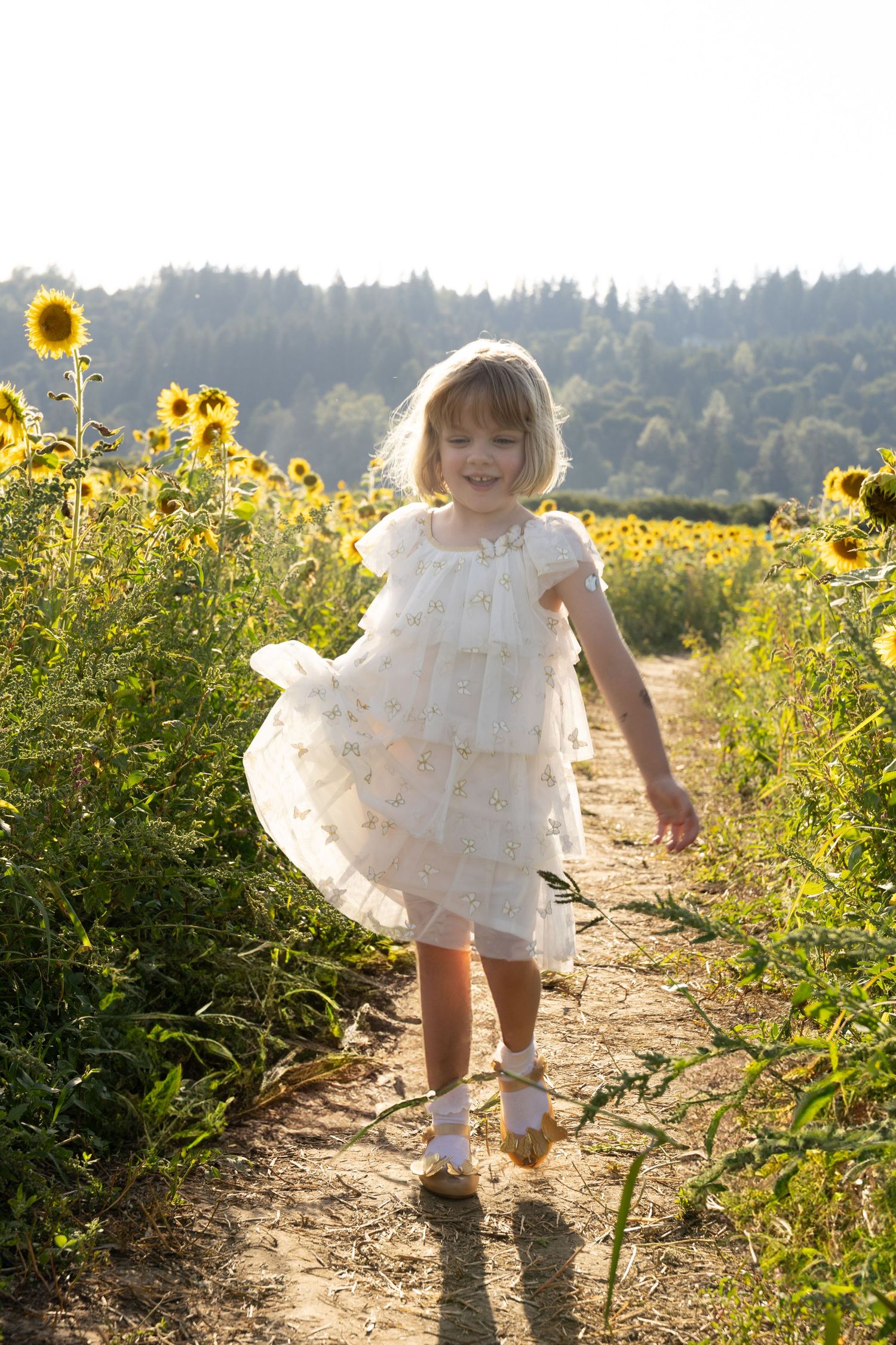 Young girl in white dress running joyfully through a sunflower field on a sunny day.