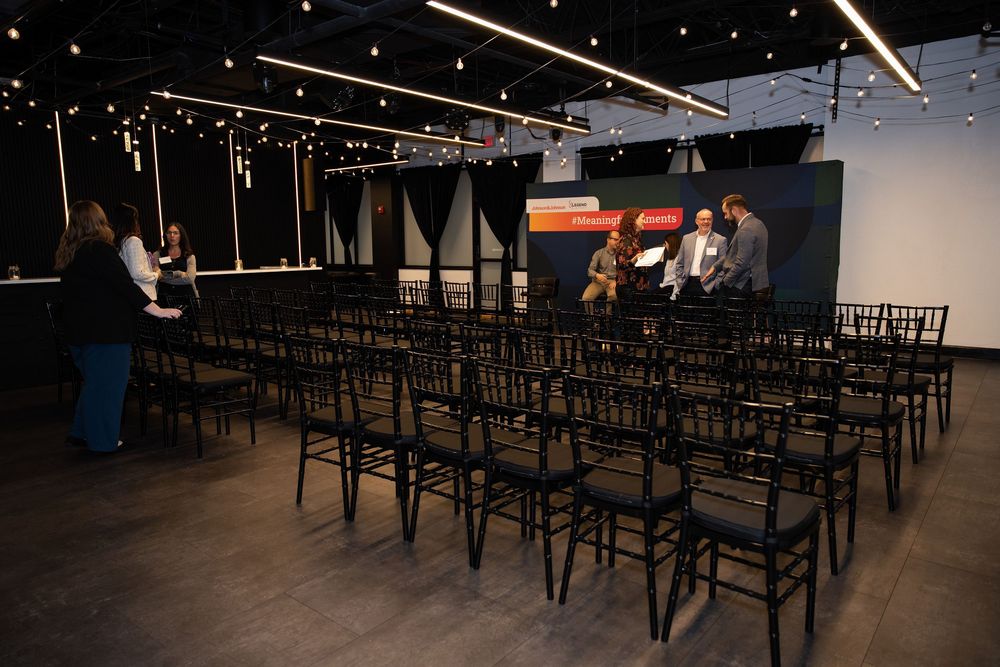 Event venue with rows of black chairs facing a small stage where panelists are seated during a conference.