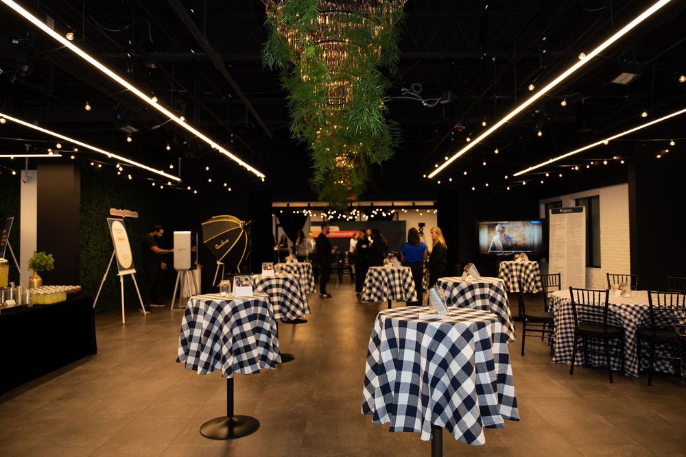 Elegant event venue with checkered tablecloths, string lights, and a lush floral chandelier in a modern black interior.