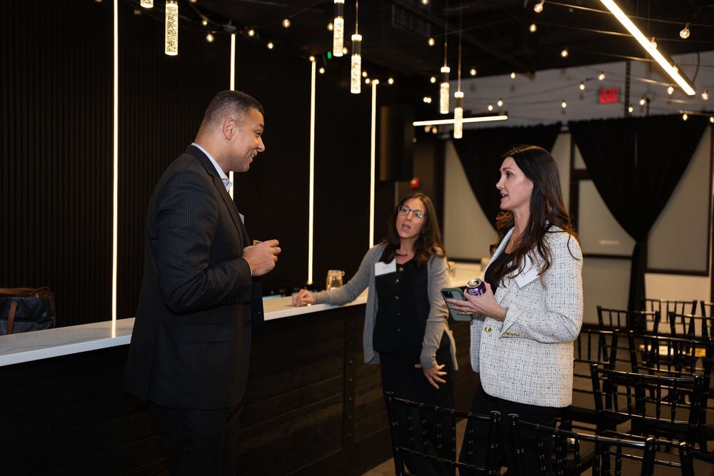 Three professionals networking at an elegant event venue with modern pendant lighting and dark decor.