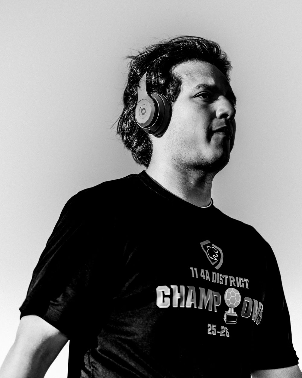 Young man wearing Beats headphones poses in black District Champions t-shirt.