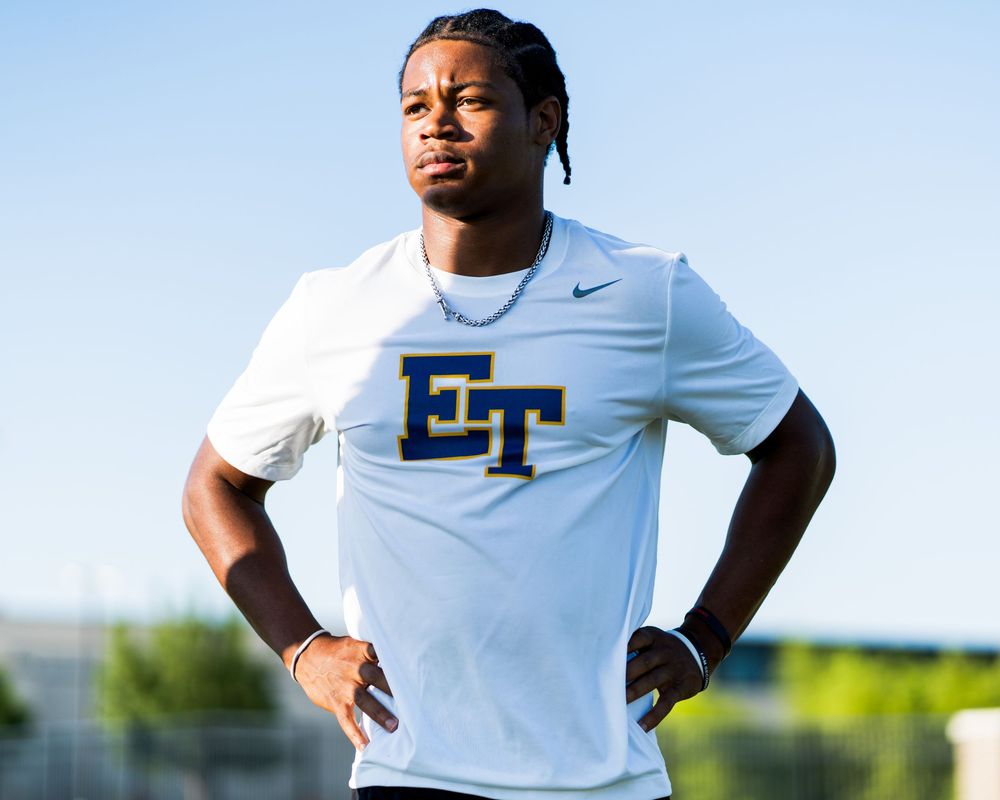 Young male athlete in white ET Nike shirt poses outdoors.