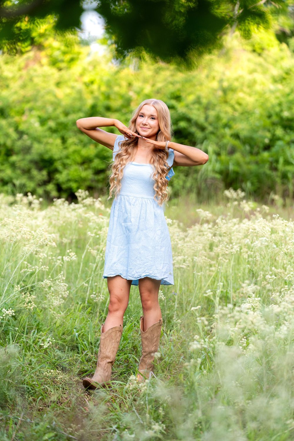 Blonde girl in blue dress and cowboy boots stands in wildflower field.