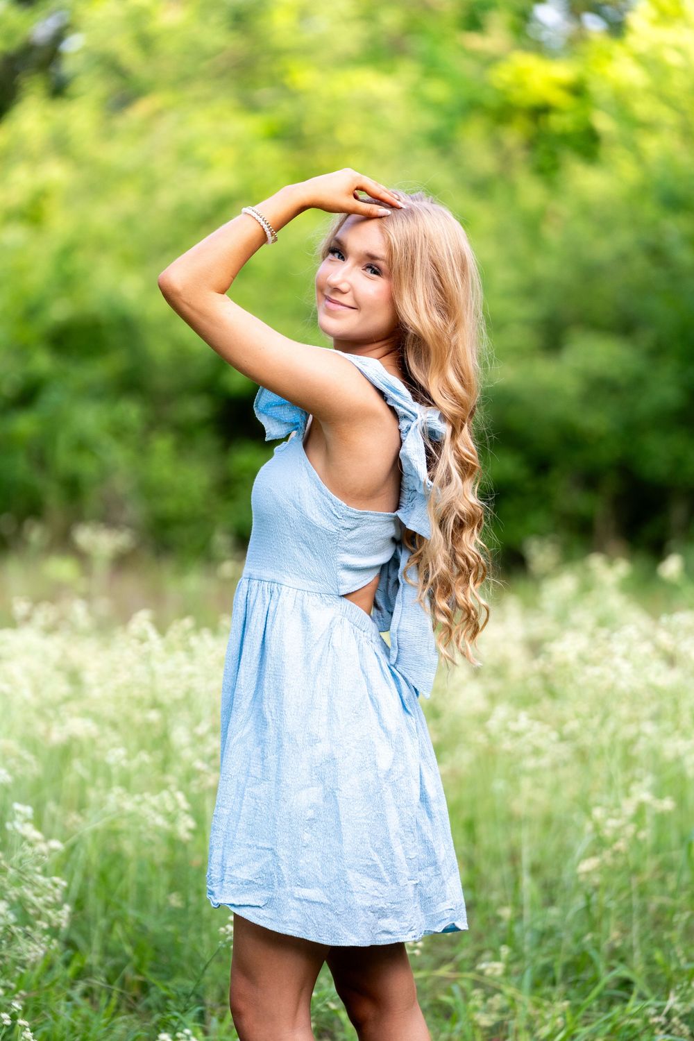 Blonde teen in blue dress poses in green meadow with wildflowers.