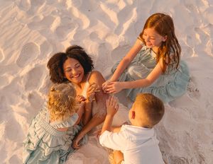 A joyful multiracial family with two women and two young children playing together on white sandy beach.