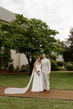 Bride and groom posing together on lawn, bride in white gown with long veil.