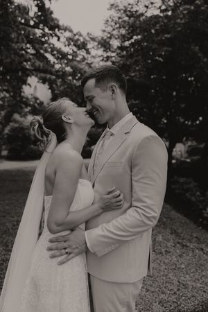Black and white photo of bride and groom leaning in for a kiss while embracing in an outdoor garden.