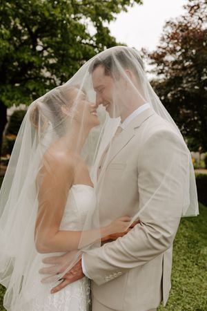Bride and groom share a romantic moment under a sheer wedding veil outdoors.