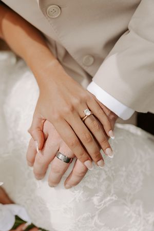 Close-up of newlyweds hands showing diamond engagement ring, gold wedding band, and silver groom wedding ring.
