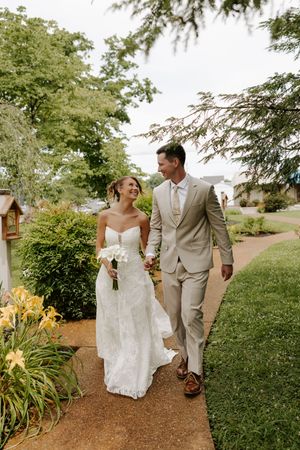 Bride and groom walking hand in hand through a lush garden pathway on their wedding day.