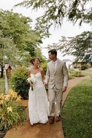 Smiling bride and groom walk hand-in-hand along garden path lined with yellow day lilies.