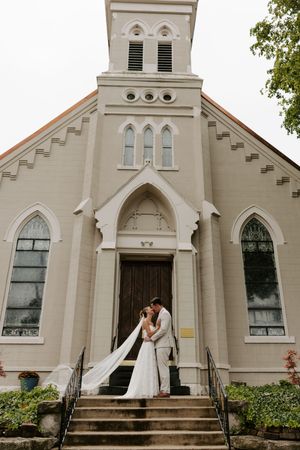 Bride and groom sharing a kiss on the steps of a historic white church on their wedding day.