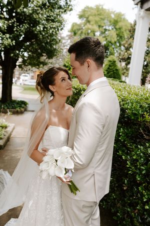 Bride and groom share romantic moment outdoors, she holds calla lily bouquet in elegant white attire.
