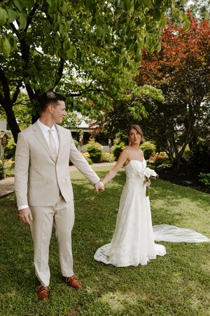 Bride and groom holding hands walking through green garden on wedding day.