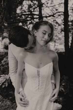 Black and white romantic photo of groom kissing bride on the neck as she closes her eyes contentedly.