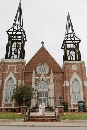Bride and groom stand on steps before grand brick Gothic church with twin spires.