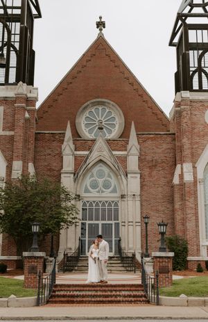 Newlyweds share a romantic moment on the steps of a beautiful red brick Gothic-style church entrance.