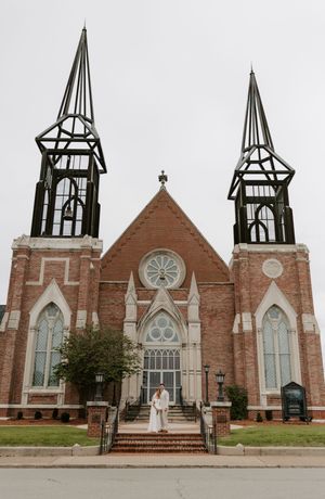 Bride and groom pose on steps of grand brick Gothic church with twin decorative spires.