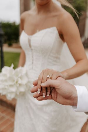 Close-up of bride and groom holding hands, showcasing the bride's diamond engagement ring and wedding band.