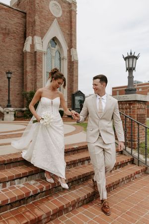 Bride and groom walking down brick church steps holding hands on wedding day.