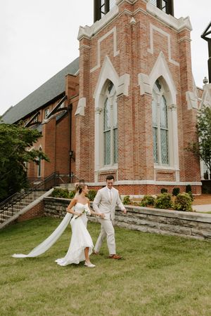 Bride and groom strolling hand in hand in front of Gothic brick church.