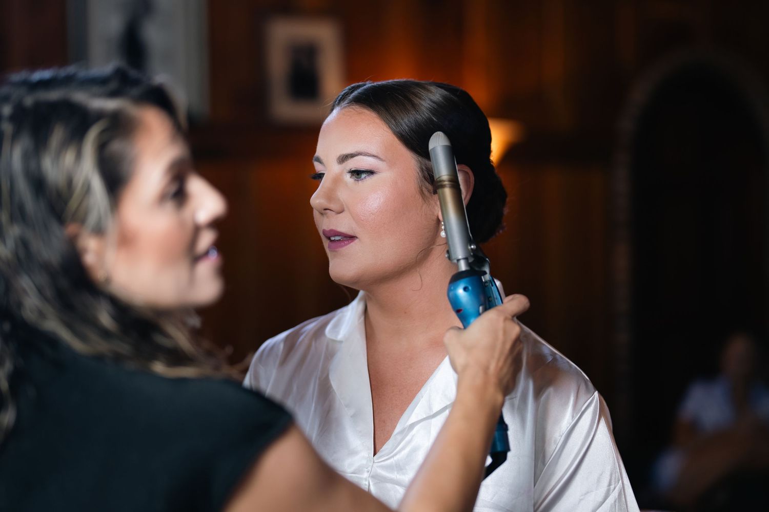 Hairstylist curling bride's hair with a curling iron as she prepares for her wedding day.