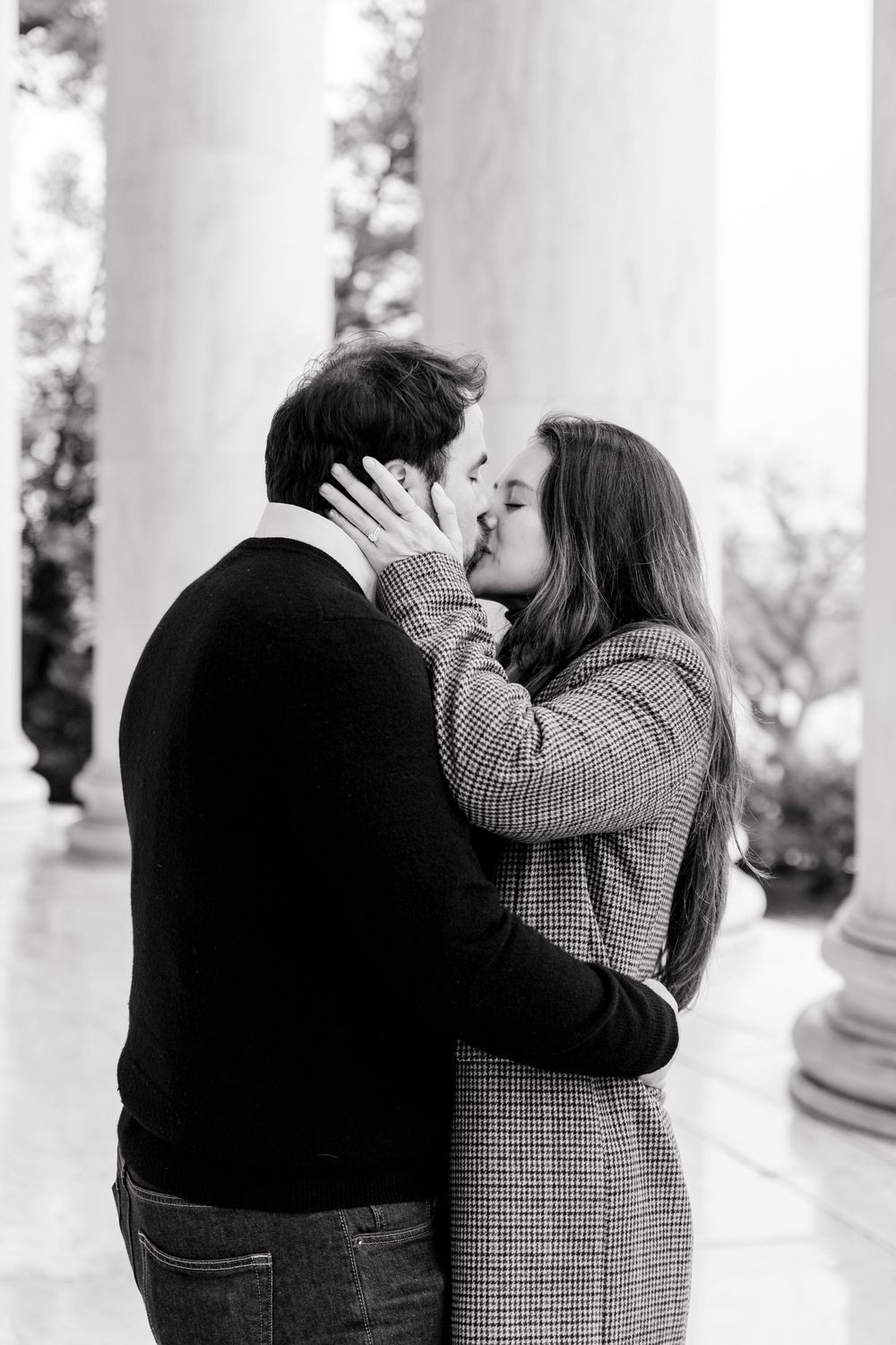 Black and white photo of a couple sharing a romantic kiss between white columns.