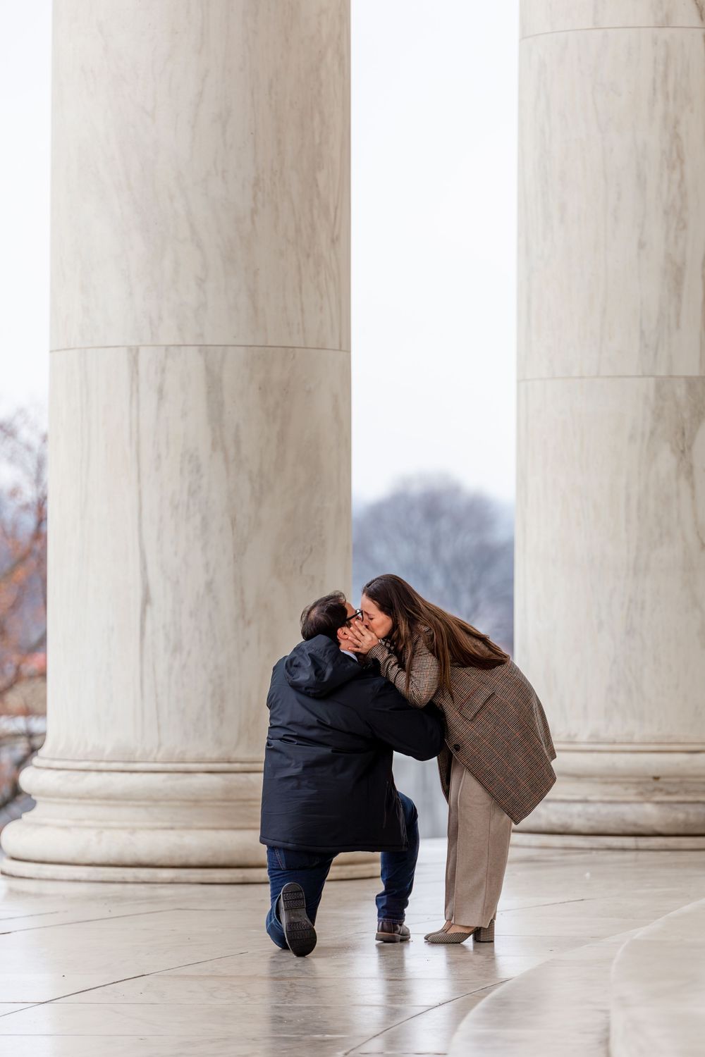 Man proposes on one knee to woman between marble columns at Jefferson Memorial, Washington DC.
