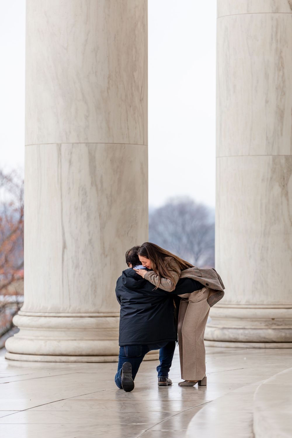 Couple embracing during a romantic marriage proposal between marble columns at the Jefferson Memorial in Washington DC.